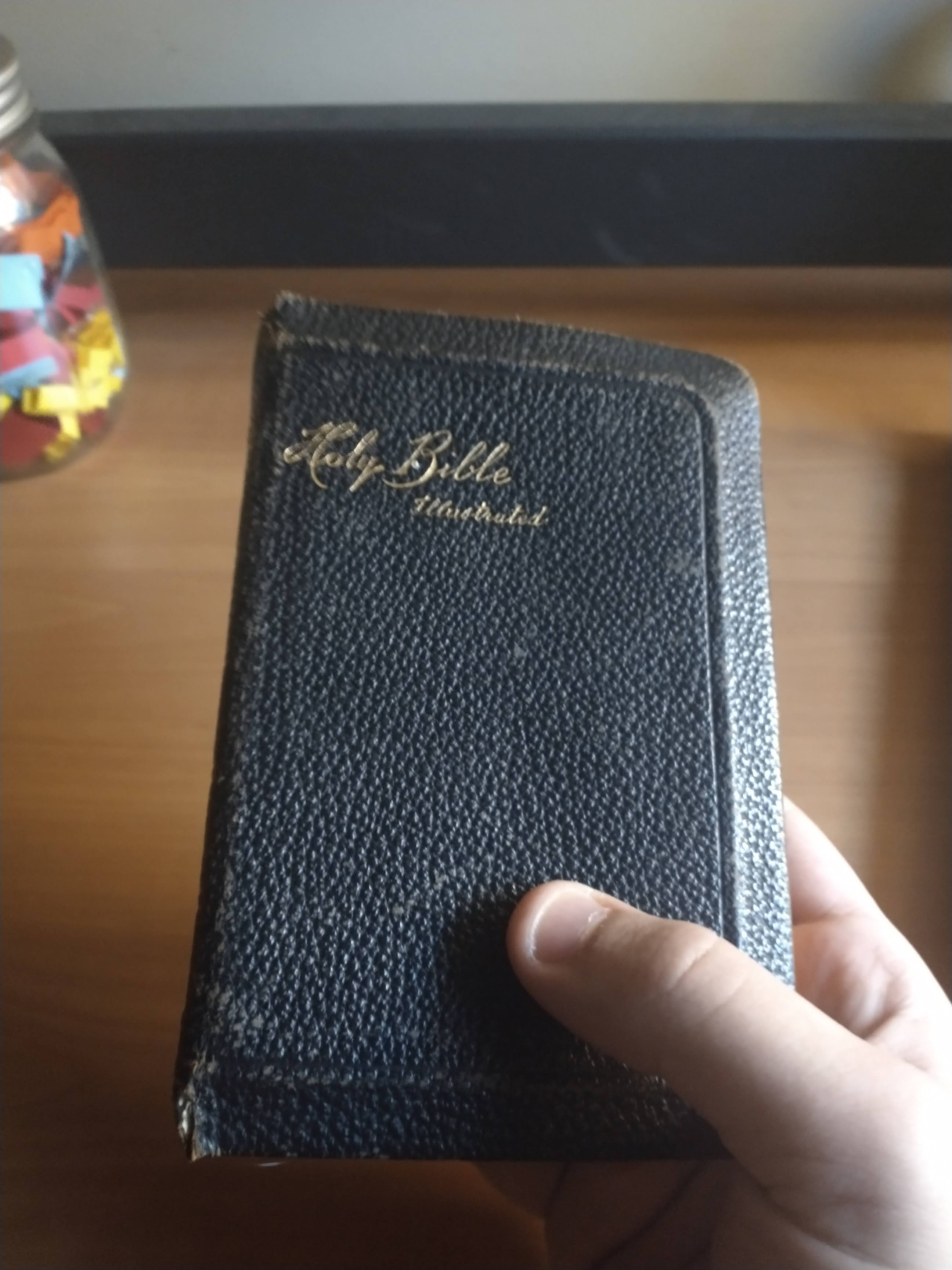 A picture of me holding the Bible in my hand. It is about the height of a smartphone, and maybe a bit wider. It is a beat-up, dirty black leather. At the top of the book, in muted, cursive gold text, it reads, "Holy Bible Illustrated".