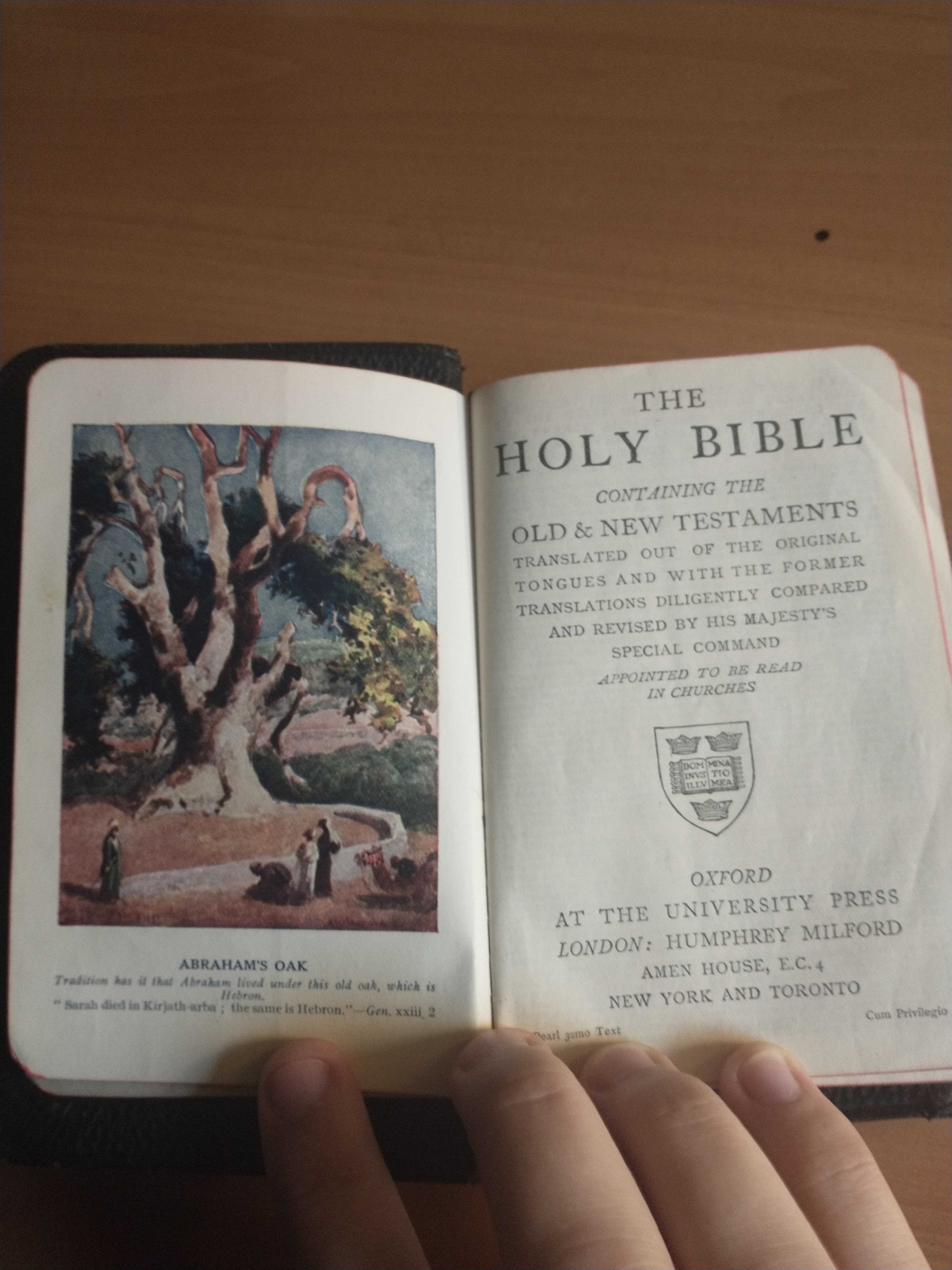 The Bible is open to its first page. On the left page is a color illustration of "Abraham's Oak". The colors are bright, almost like watercolors. There are figures gathered around the bottom of the tree. On the right page is an old-looking copyright page that reads in all-caps, "The Holy Bible, Containing The Old & New Testaments, Translated Out Of The Original Tongues And With The Former Translations Diligently Compared And Revised By His Majesty's Special Command, (in italics)Appointed To Be Read In Churches". The logo for Oxford University is printed. Then, the text continues, "Oxford, At The University Press; London: Humphrey Milford, Amen House, E.C.4, New York And Toronto".